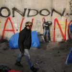 A migrant walks past a wall with a graffiti mural representing Steve Jobs by British artist Banksy in the "new jungle", a field where migrants and asylum seekers stay in Calais